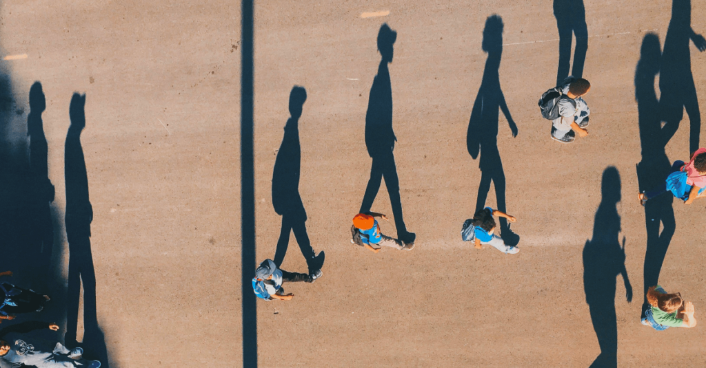Imagem aérea exibindo pessoas caminhando, sendo que suas sombras se alongam ao lado delas